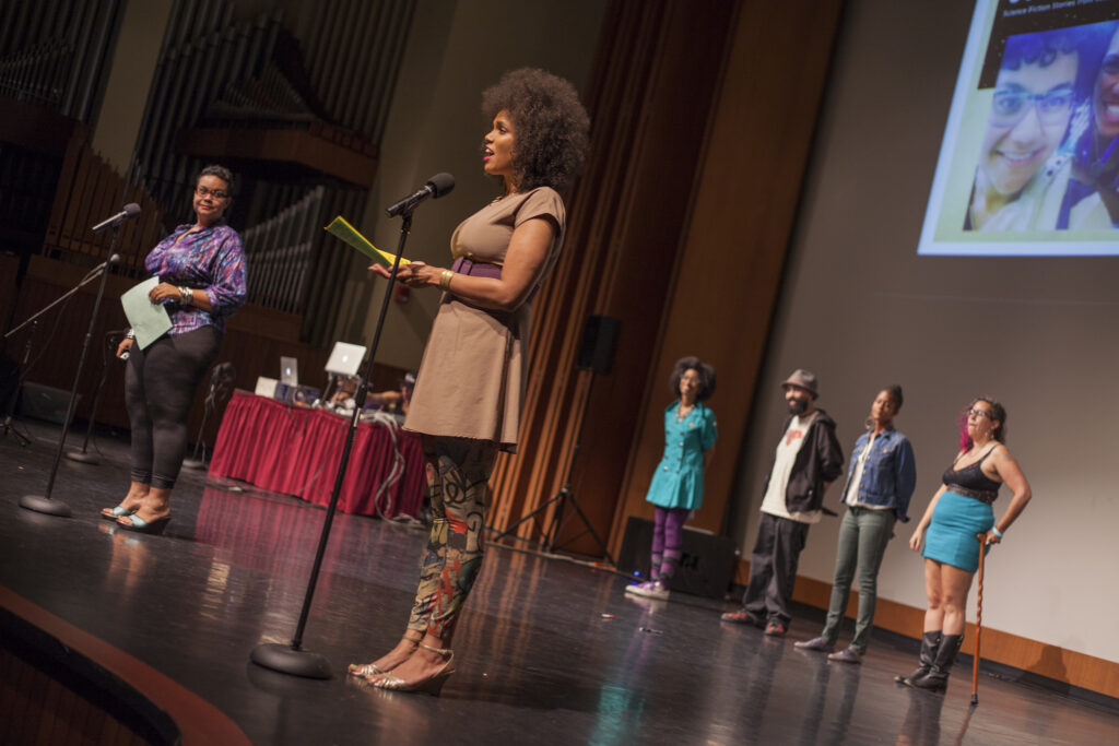 Two presenters on stage at the AMC standing at mics, with four people behind them at the back of the stage