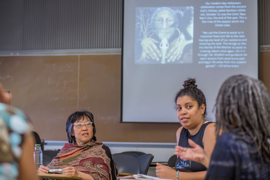 Three participants of Radical Crones in a discussion in front of a chalkboard and projector screen