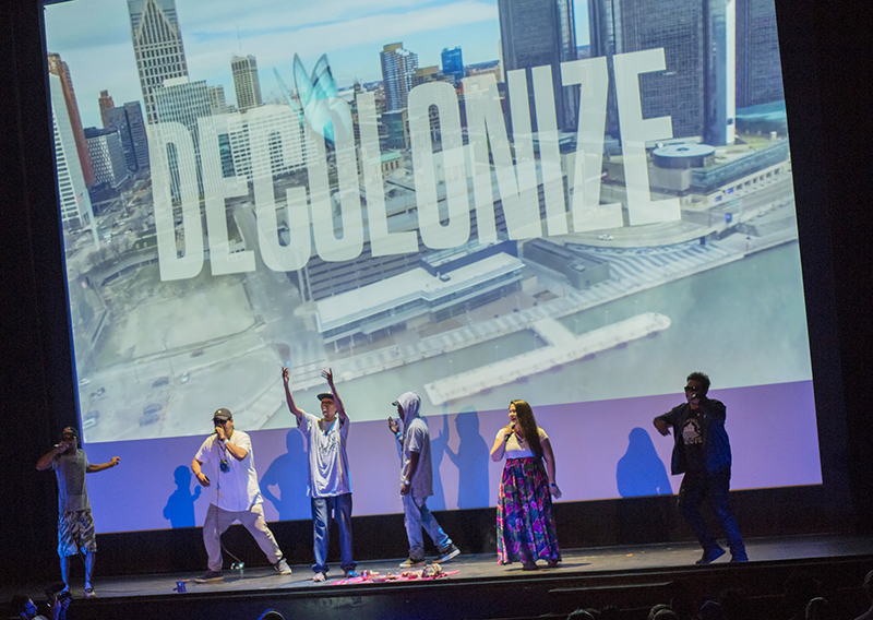 Opening stage of the 2017 AMC with performers on stage infront of a backdrop with the word "Decolonize"