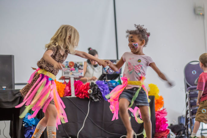 Two face-painted kids dancing together in front of a DJ