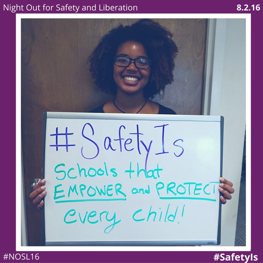 A young Black woman holding a sign that says "#SafetyIs Schools that empower and protect every child!"