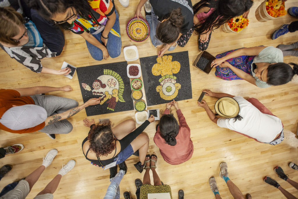 Overhead perspective of people on the floor making illustrations on black paper using beans