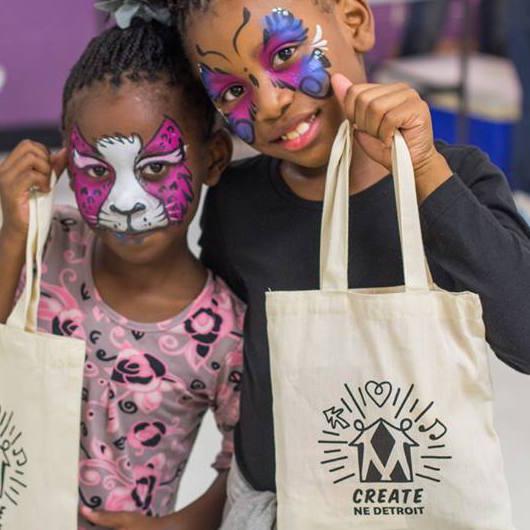 Two Black girls with face paintings holding Create NE Detroit tote bags