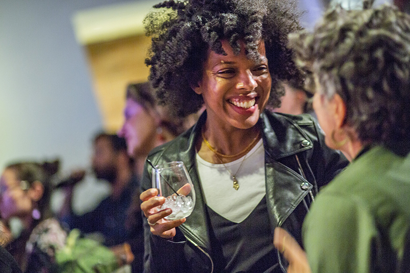 An attendee of the AMC holding a drink with a big smile, listening in a conversation