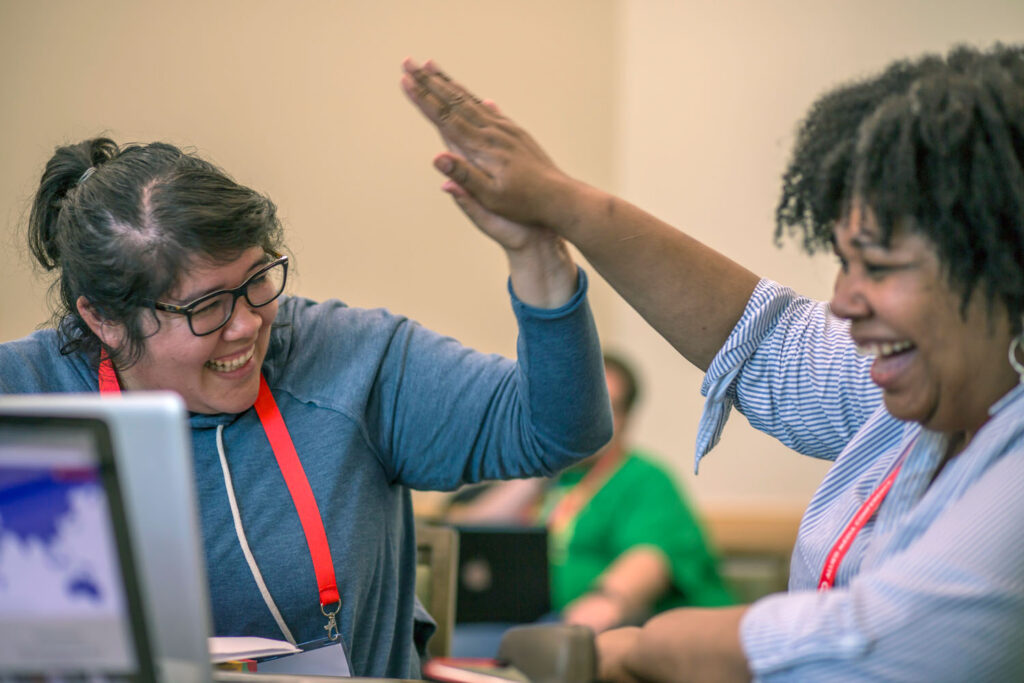 Two AMC attendees sitting at a table smiling and high fiving each other