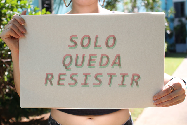 Person holding a sign that says "SOLO QUEDA RESISTIR"