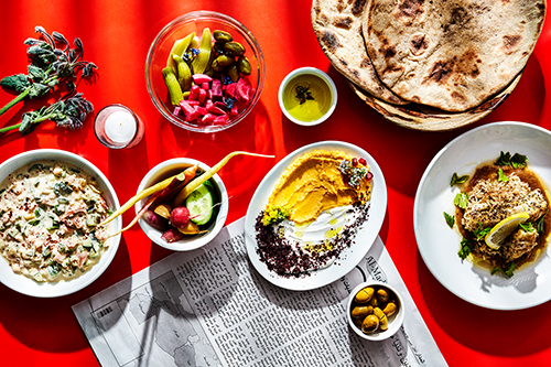 Overhead shot of mediterranean food on a red table with a newspaper