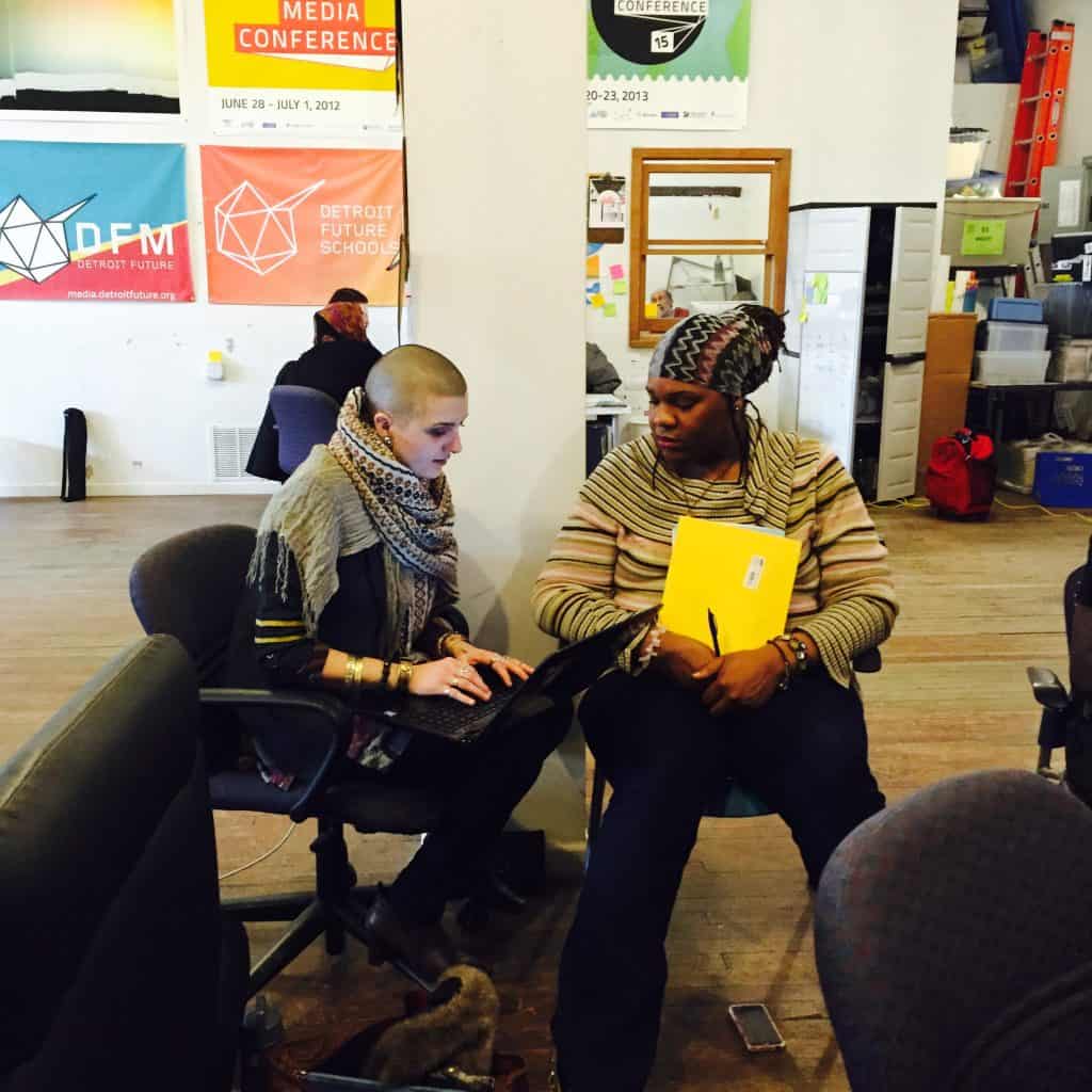 Two people sitting together on roller chairs at the AMP office with one typing on a laptop on their lap