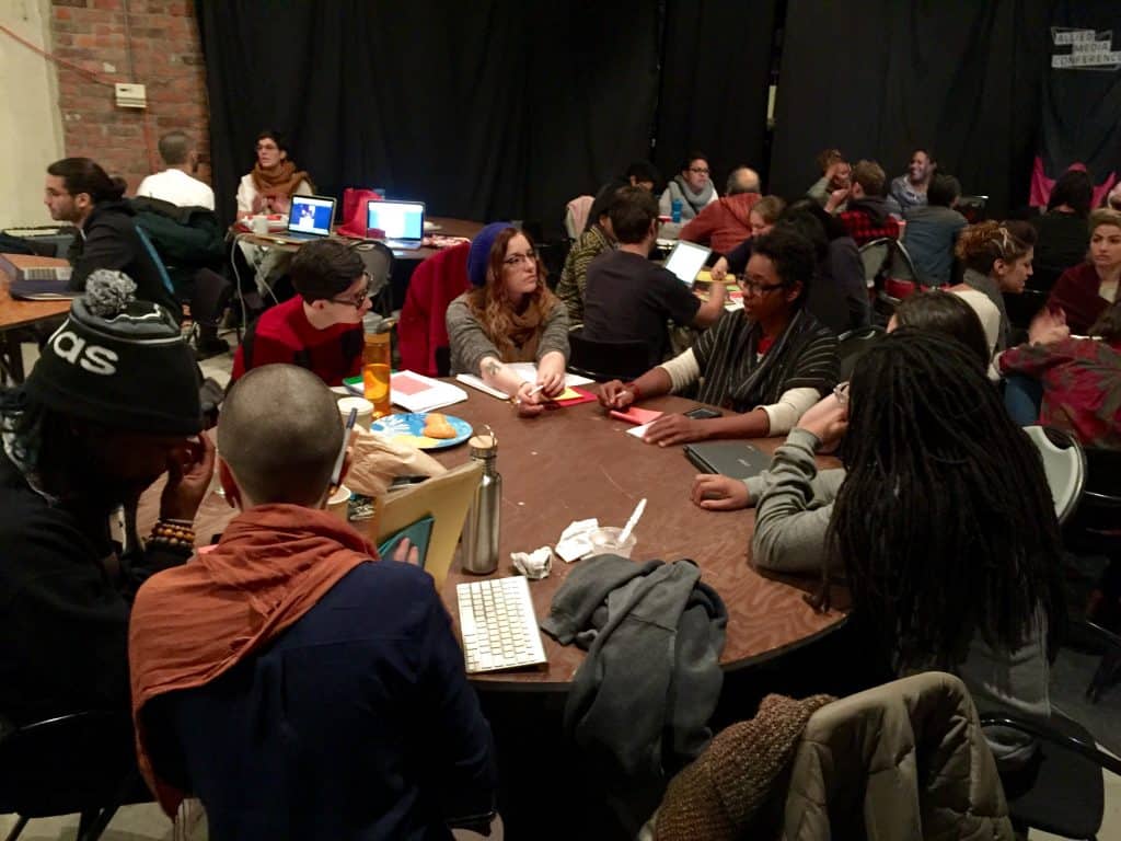 A room with a few round tables and groups of people sitting around them discussing