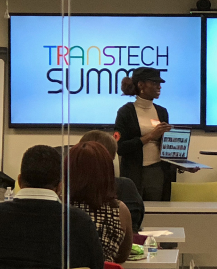 Photo of person holding a computer with a Trans Tech Summit behind 