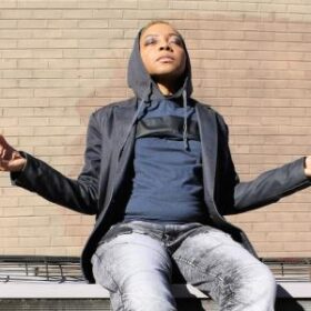 Photo of a Black woman sitting outside with eyes closed and face to the sky and arms out to the side