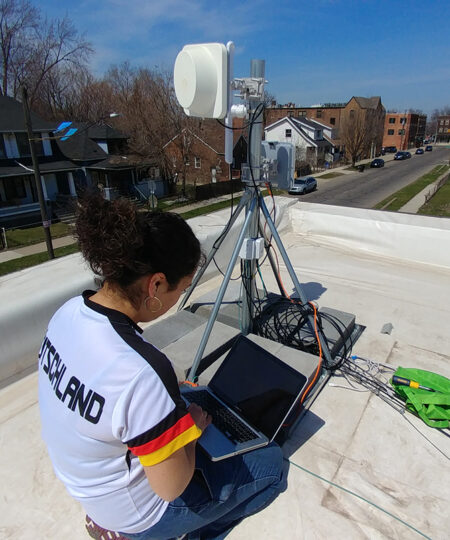 person sitting on a roof with a laptop and wireless networking equipment