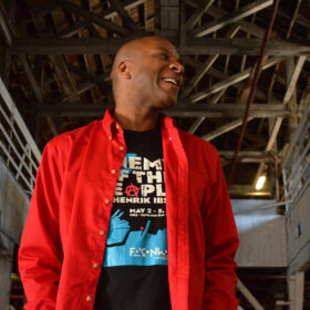 photo of reg flowers, smiling and wearing a red button-up shirt over a black t-shirt