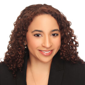 headshot of Dana Britto against a white background, wearing a black blazer jacket