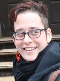 Headshot of Hannah Sassaman wearing red earrings and gray scarf