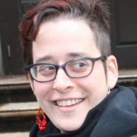 Headshot of Hannah Sassaman wearing red earrings and gray scarf