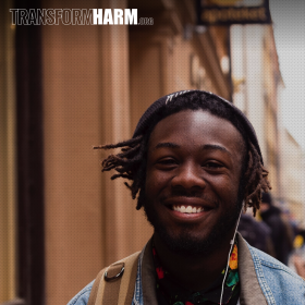 Portrait photo of a young black man on a city sidewalk, smiling with headphones with the headline text "TranformHarm.org"